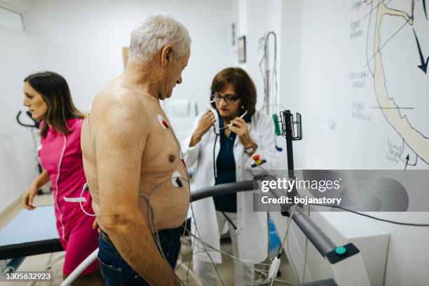 rijpe vrouwelijke arts die stethoscoop op hogere mannelijke patiënt gebruikt terwijl het hebben van de test van de hartstress op loopband bij cardiologiekliniek - womans clinic heart stockfoto's en -beelden