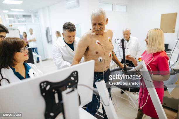 groep cardiologen die hartstresstest op een loopband van een hogere mannelijke patiënt controleren - treadmill test stockfoto's en -beelden