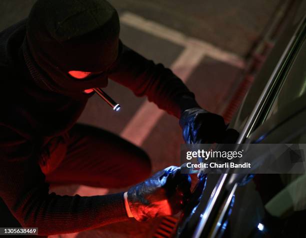 disguised thief, holding the flashlight in his mouth while trying to unlock the car door with screwdriver - screwdriver stock pictures, royalty-free photos & images