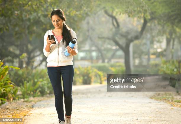woman in sportswear using phone while walking at park - tracksuit top stock pictures, royalty-free photos & images