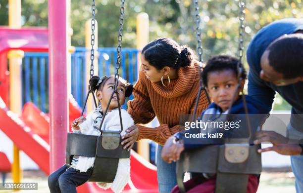 junge familie mit zwillingen auf spielplatzschaukeln - mother and son at playground stock-fotos und bilder