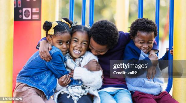 vier junge geschwister umarmen sich auf spielplatz - african american children playing stock-fotos und bilder