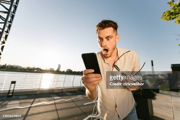 hombre conmocionado leyendo mensaje al aire libre - surprise fotografías e imágenes de stock
