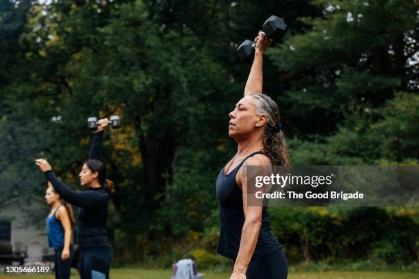 mature woman working out with dumbbells during outdoor fitness class - entraînement-aux-haltères photos et images de collection