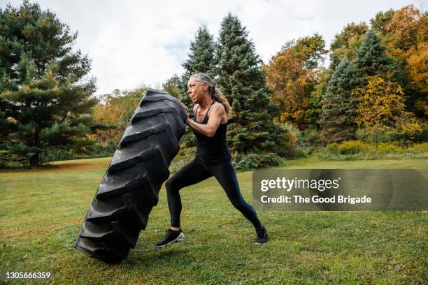 strong woman pushing tire while exercising in backyard - mujeres musculosas fotografías e imágenes de stock