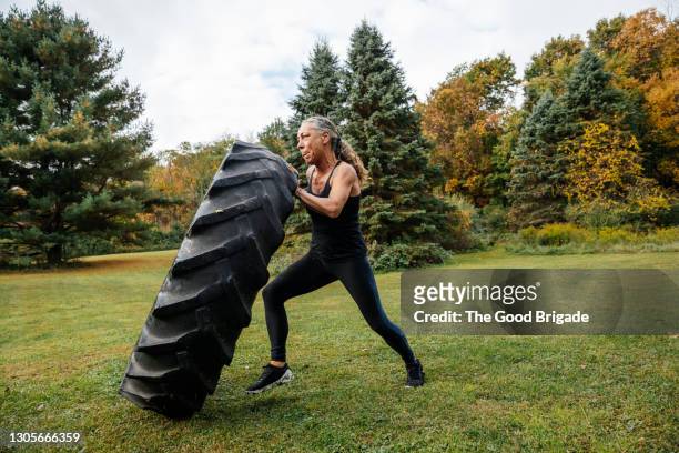 strong woman pushing tire while exercising in backyard - strong woman stock pictures, royalty-free photos & images