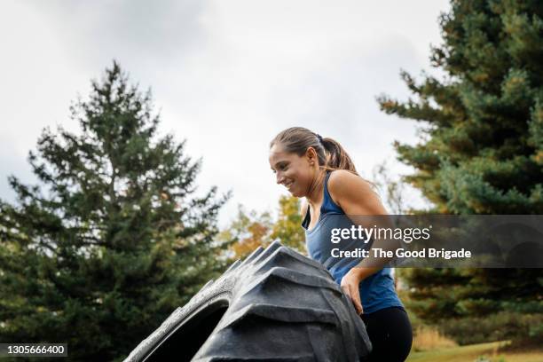 young female athlete picking up tire during exercise class outdoors - autoreifen natur stock-fotos und bilder