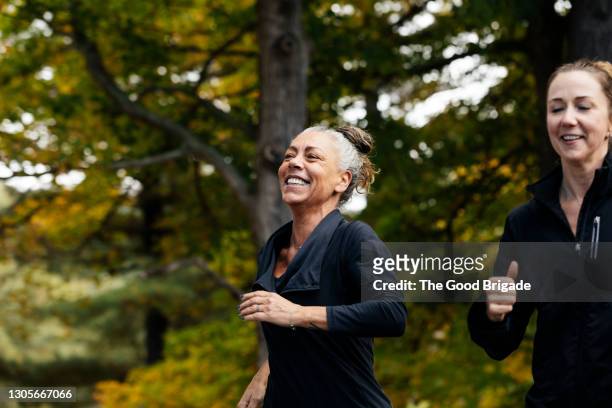 cheerful mature woman with female friend jogging in forest - women working out stock pictures, royalty-free photos & images