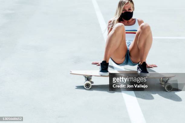 blonde woman in shorts and mask lying on the floor with her feet on top of her longboard skateboard. - figure skater stockfoto's en -beelden