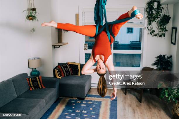 a women hangs upside down from her aerial silk that is setup in the living room of her home - draped stockfoto's en -beelden