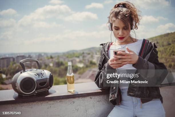 young girl in retro style on the roof of the building spends her time and enjoys the moment - listens to music on the roof of the building, enjoys freedom and drinks alcohol - girls boom box stock pictures, royalty-free photos & images