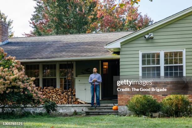 man holding broom standing on front porch at home - stéréotype de la classe moyenne photos et images de collection