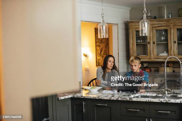 mother helping son with homework while sitting at kitchen counter - parental control stock pictures, royalty-free photos & images