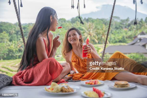 asian lesbian couple eating breakfast on a large  hanging daybed at holiday villa - bali volcano stock pictures, royalty-free photos & images
