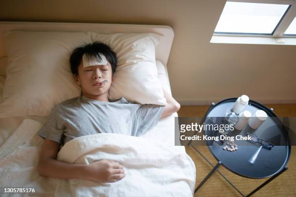 asian chinese sick teenager lying on bed with thermometer in his mouth measuring body temperature - hot boy body stock pictures, royalty-free photos & images