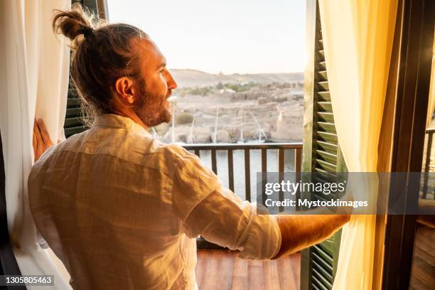 man opening curtains in hotel room at sunrise, nile river - green curtain stock pictures, royalty-free photos & images