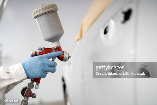 close-up image of car painter with protective clothes and mask painting car using spray compressor in auto repair shop. - エアブラシ ストックフォトと画像