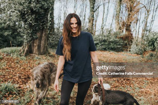 gorgeous young woman with fabulous gap toothed smile walking her dogs through a forest. she smiles directly at the camera. - frauen hund park stock-fotos und bilder