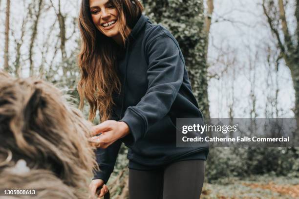 gorgeous young woman with fabulous gap toothed smile bends down to pet her large dog who is in the foreground - parklücke stock-fotos und bilder