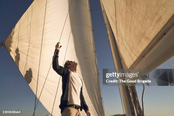 man looking up at sails while standing on boat - vela foto e immagini stock