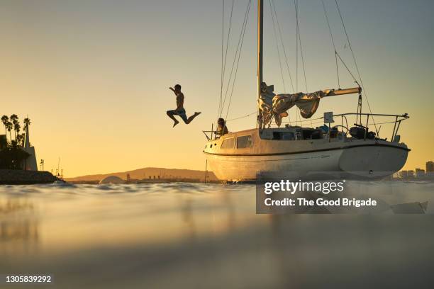 man jumping into ocean from deck of sailboat at sunset - den sprung wagen stock-fotos und bilder