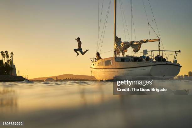 man jumping into ocean from deck of sailboat at sunset - yacht bildbanksfoton och bilder