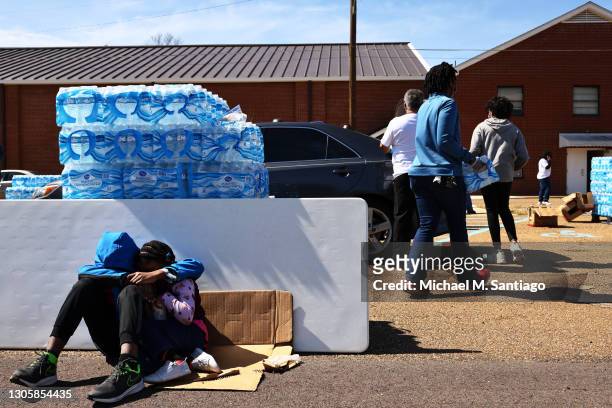 Jonathan Thomas and his sister Journey shade themselves from the sun as they play on an iPad while their mother Alicia Thomas volunteers at a water...