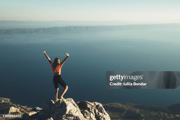 young woman standing on cliff's edge - woman cliff stock pictures, royalty-free photos & images