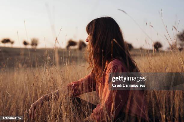 hermosa joven disfrutando de la luz del sol mientras se sienta en la hierba alta - blusa beige fotografías e imágenes de stock