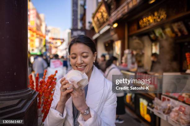 young woman eating steamed dumpling on street - yokohama imagens e fotografias de stock