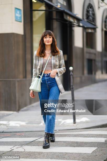 Influencer Dolorescfr wears a checked pattern blazer jacket, a gray crop top, a green leather bag, blue denim jeans pants, black shiny leather boots...