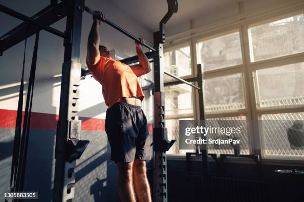 jonge mens die pull-ups in een gymnastiek doet - chin ups stockfoto's en -beelden