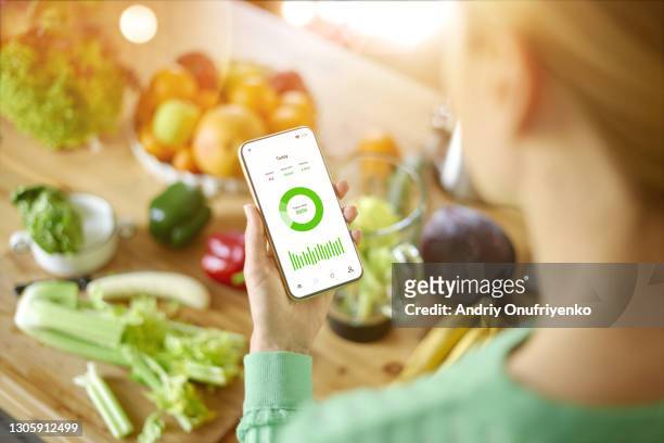 young beautiful woman watching mobile health activity application over table with vegetables and fruits. - raw food diet stockfoto's en -beelden