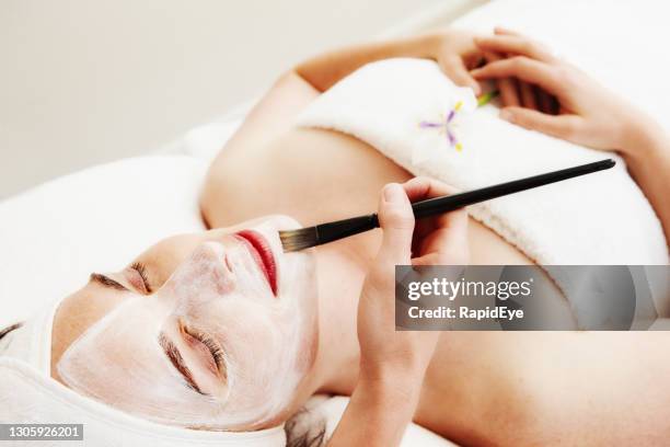 schöne junge frau mit einer gesichtsmaske von einem therapeuten in einem beauty-spa gemalt - kosmetik gesicht pinsel stock-fotos und bilder