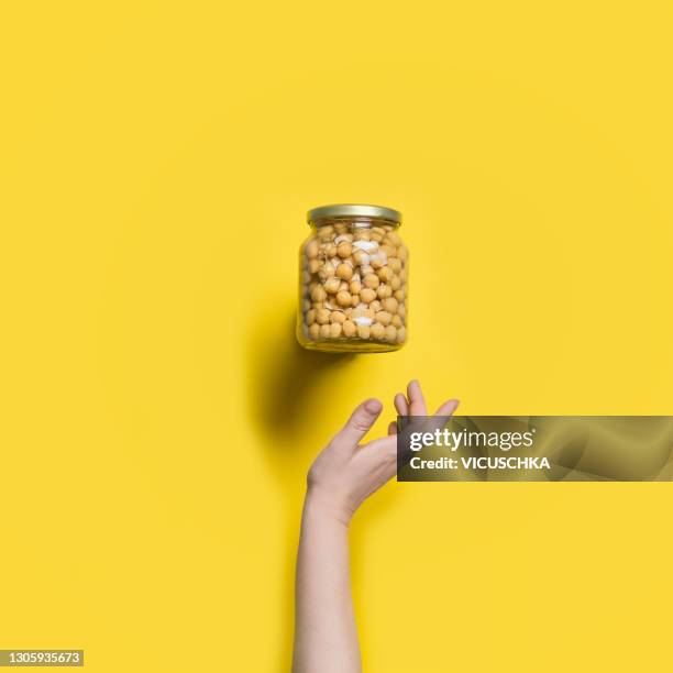 flying glass jar with canned chickpeas and woman hand at yellow background. - canned goods stock-fotos und bilder