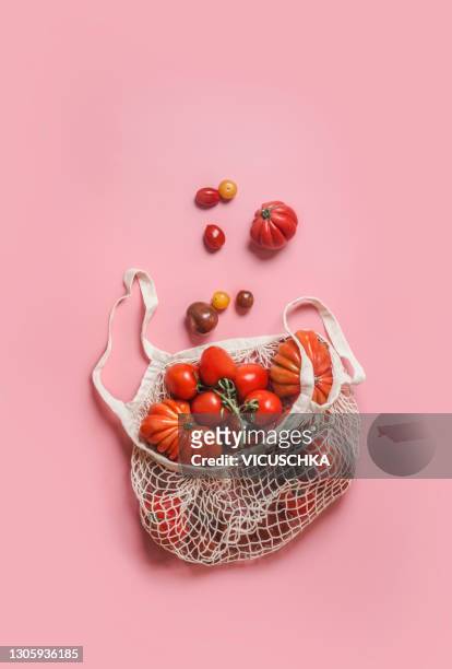 white eco-friendly shopping mesh bag with various colorful tomatoes at pink background. top view. - tomate fotografías e imágenes de stock