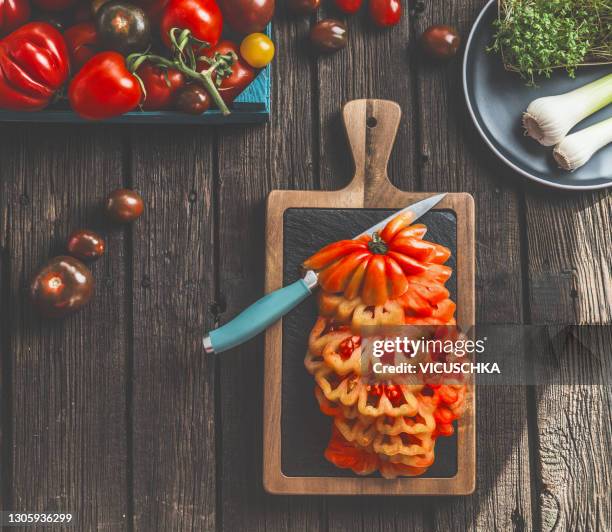 sliced big beefsteak tomato with knife on cutting board  on wooden rustic kitchen table background - beefsteak tomato stock pictures, royalty-free photos & images