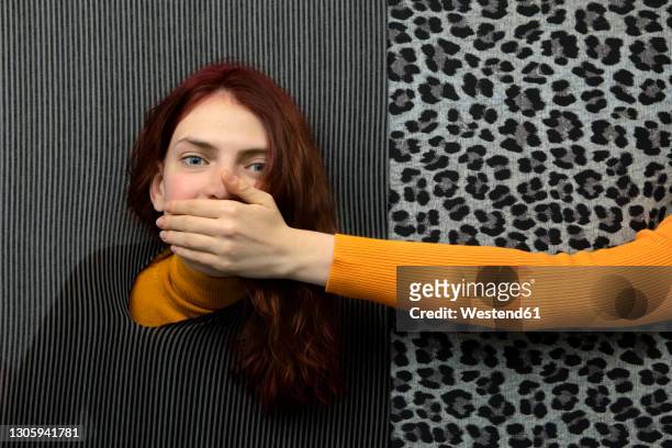 studio shot of female hand covering mouth of young redhead woman - hands covering mouth stockfoto's en -beelden