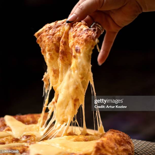 melted cheese stretches on slice of hot pizza. woman takes a slice of pizza. delicious pizza. traditional italian food, close up shot. nutrition dinner or lunch - vegetarian pizza stock-fotos und bilder