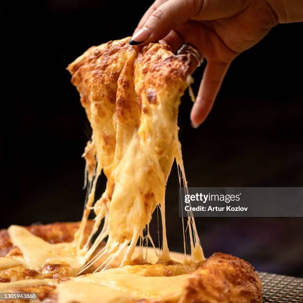 melted cheese stretches on slice of hot pizza. woman takes a slice of pizza. delicious pizza. traditional italian food, close up shot. nutrition dinner or lunch - ピザ ストックフォトと画像