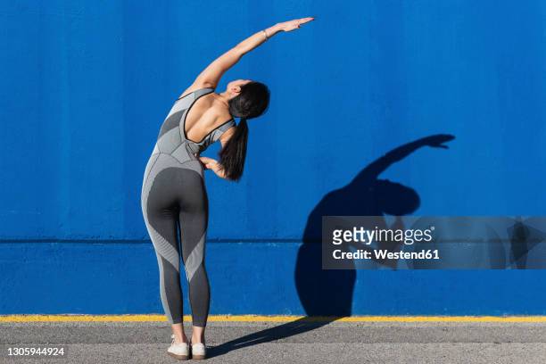 woman in sports clothing doing exercise in front of blue wall - braccio umano foto e immagini stock