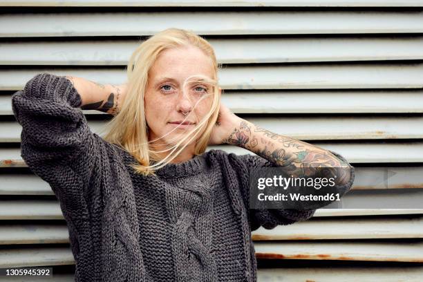 tattooed woman with hand in hair standing in front of shutter - sommersprossen stock-fotos und bilder