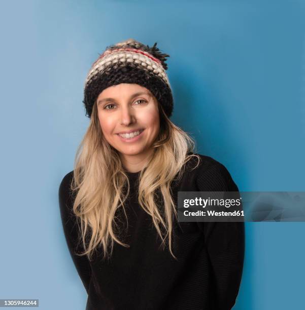 smiling blond woman in knit hat against blue background - wollmütze stock-fotos und bilder