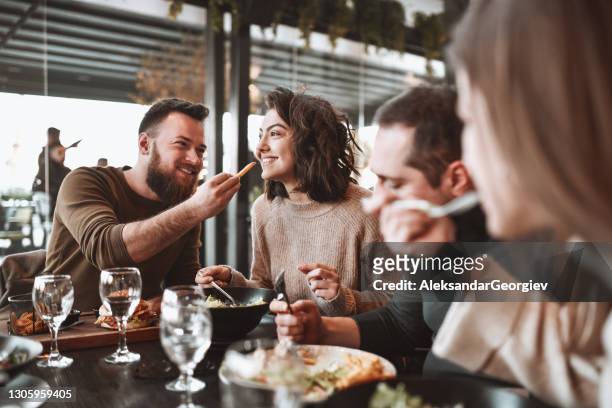 hombre alimentando a su novia mientras almorzaba con amigos en restaurante - male burger eating fotografías e imágenes de stock