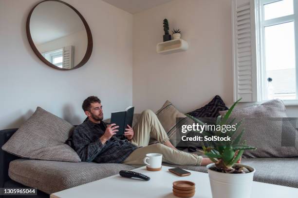bachelor relaxing and reading a book in his apartment - detox digital imagens e fotografias de stock
