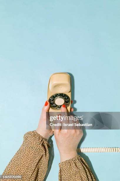 woman's hand dialing phone number on an old yellow rotary dial telephone on blue background. communication concept. - vintage telephone stock pictures, royalty-free photos & images