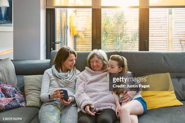 three generations of the same family laughing at something funny on the smartphone - mutter grossmutter kind stock-fotos und bilder
