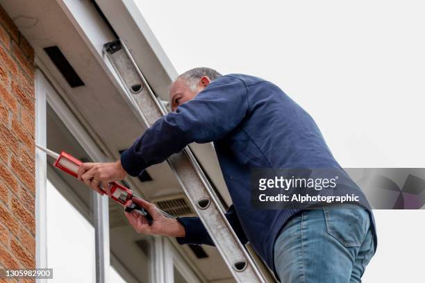 senior man putting sealant around leaking windows - january 2021 stock pictures, royalty-free photos & images