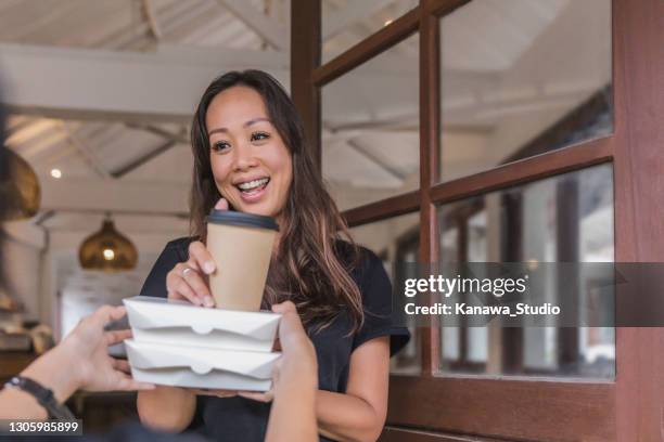 cheerful asian woman receiving take-out food and drink from courier - receiving delivery stock pictures, royalty-free photos & images