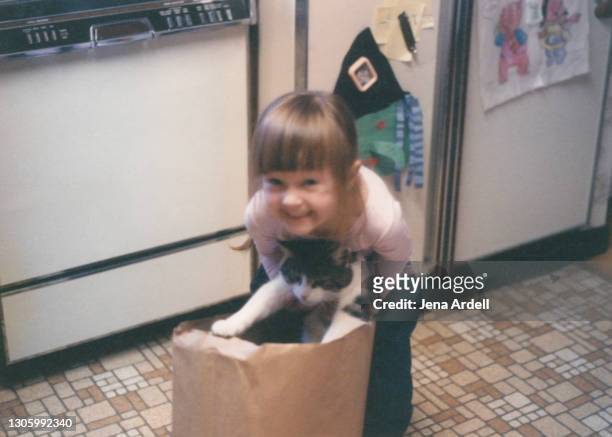cat's out of the bag: little girl holding cat, unamused cat from childhood - girls photos stock-fotos und bilder